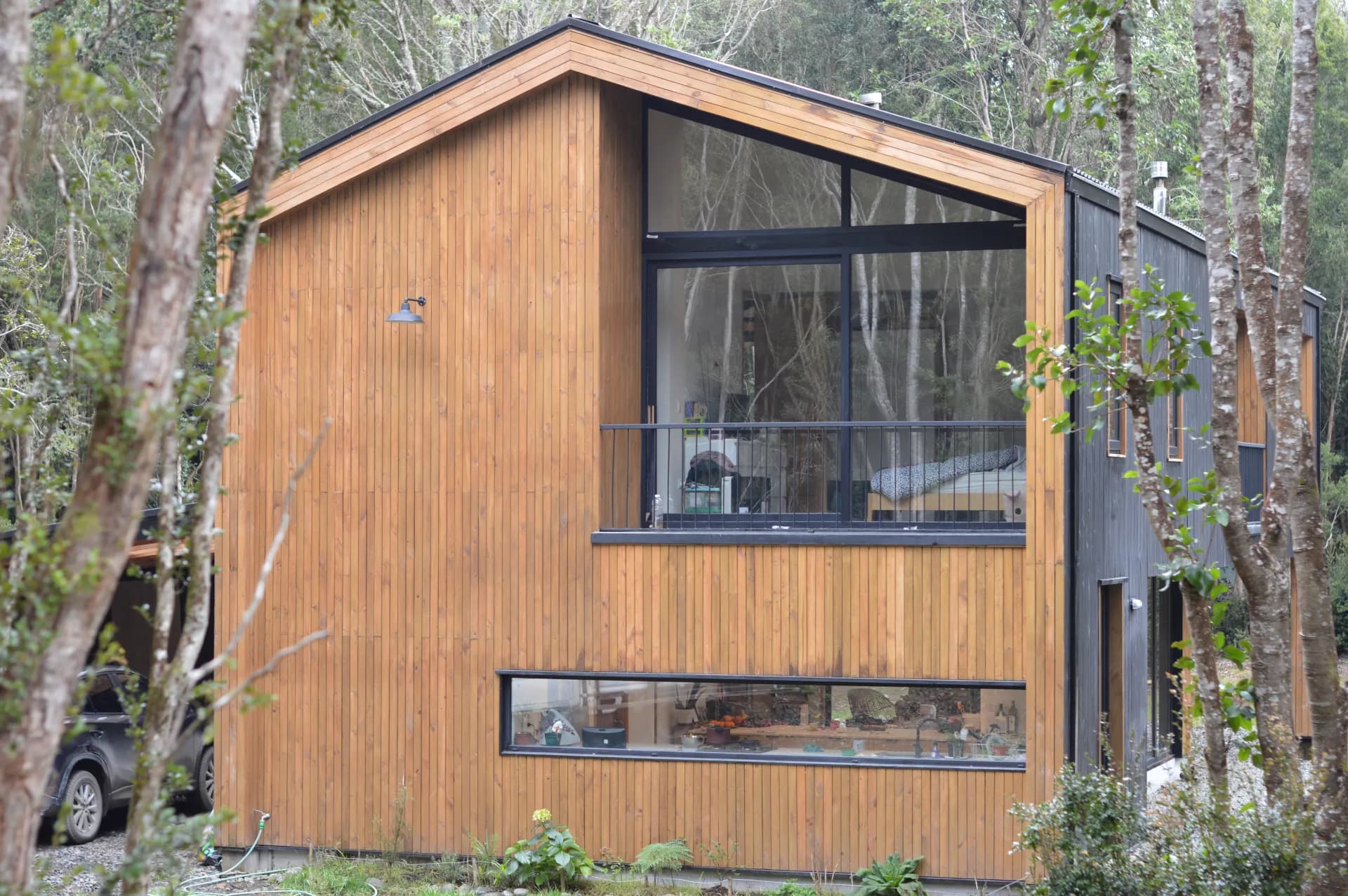 Vivienda de madera con grandes ventanales de cristal en entorno de bosque, obra de DM Cristales