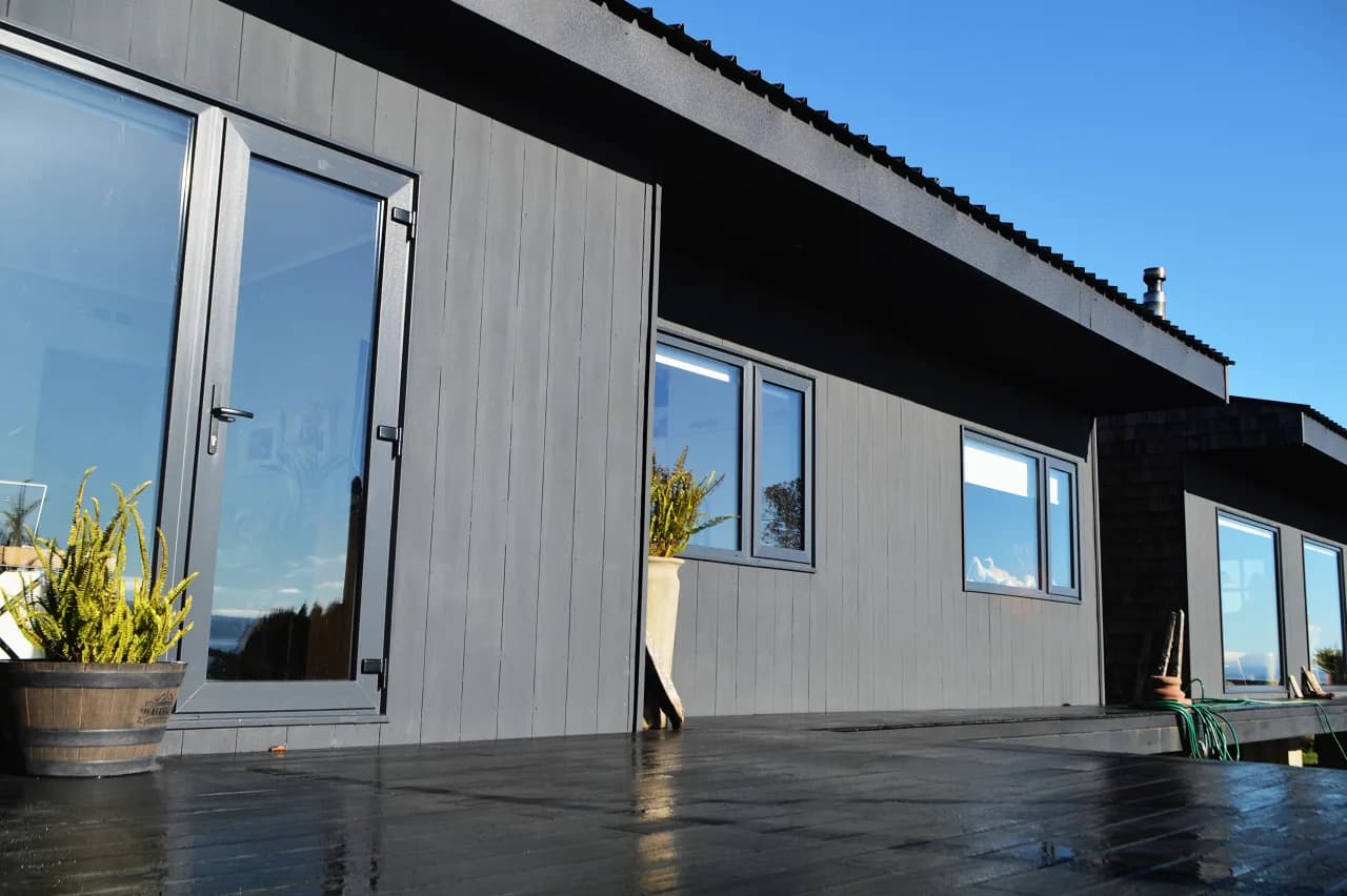 Puertas y ventanas de PVC negro en termopanel en fachada gris, obra de DM Cristales en Ensenada, Región de Los Lagos