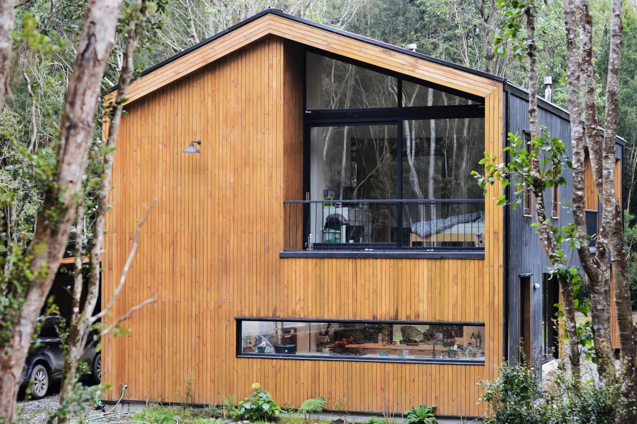 Casa con ventanas de PVC negro en termopanel y revestimiento de madera en entorno de bosque, obra de DM Cristales en la Región de Los Lagos